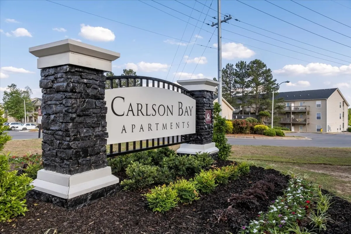 The entrance sign of Carlson Bay is prominently featured, surrounded by thoughtful landscaping and mature trees. This inviting exterior view signals a sense of place, community, and approachable living for residents and visitors alike.