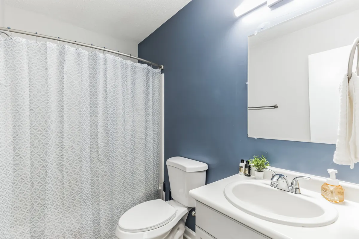 A sparkling, spa-inspired bathroom featuring a fresh shower curtain, a well-lit vanity sink with a mirror, and neatly arranged towels. The environment feels inviting and fresh, perfect for peaceful morning routines or unwinding after a long day.