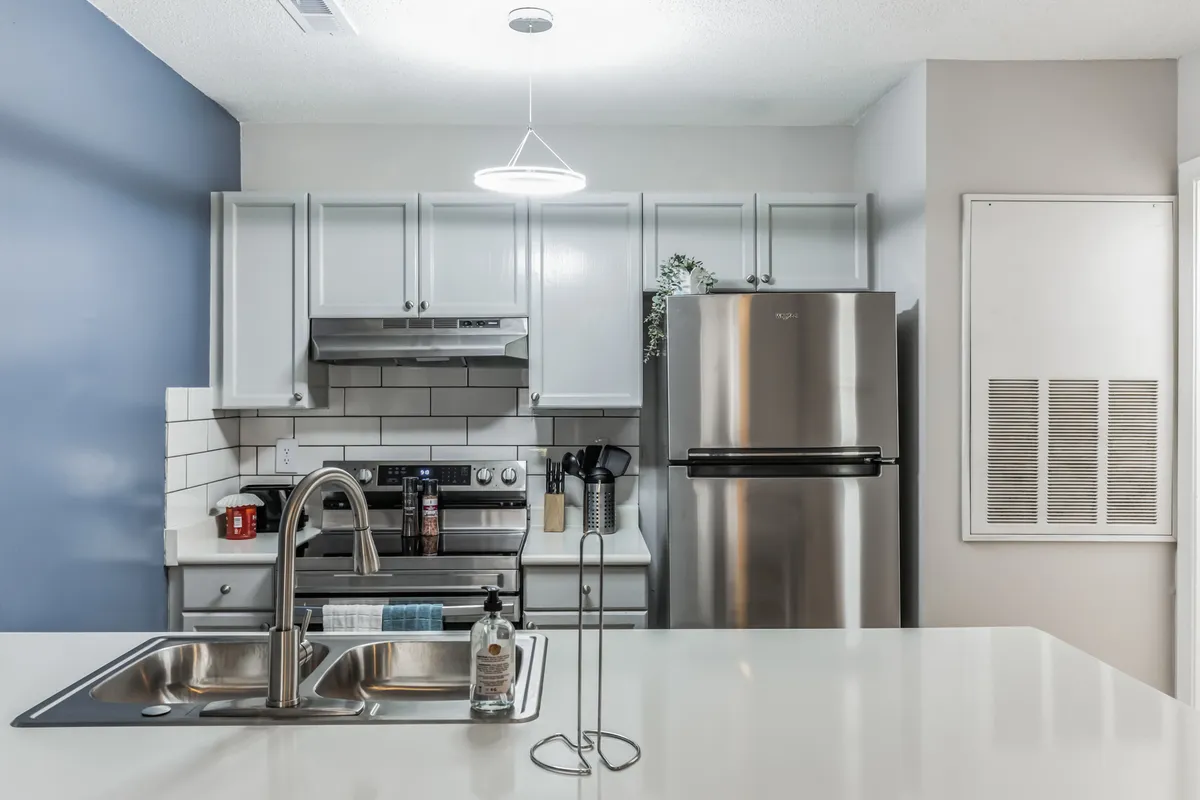 A modern kitchen featuring a spacious island, stainless steel appliances, colorful dish towels, and a warm, welcoming layout. The image highlights the kitchen's ample counter space and showcases cookware and utensils, conveying readiness for meal preparation or entertaining.