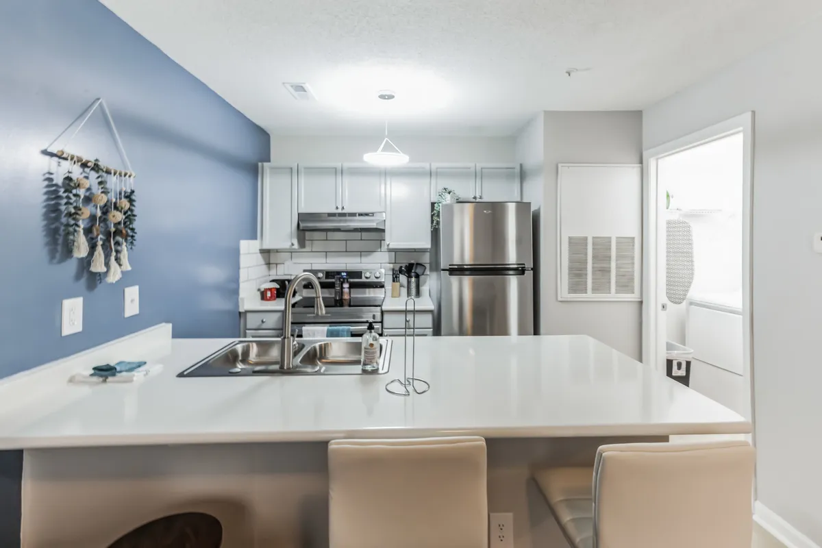 A cozy, modern kitchen with a large island, stainless steel appliances, and a blue accent wall. The space is set up for cooking, entertaining, and socializing, suggesting home-like flexibility and comfort.