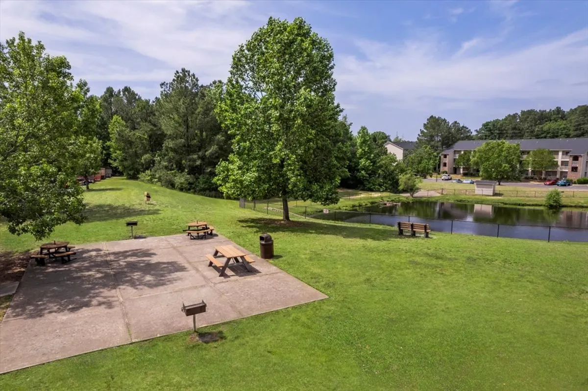 A serene picnic area by a pond, complete with benches and shaded by trees. People are seen picnicking, walking, fishing, and socializing, highlighting the variety of activities available nearby.