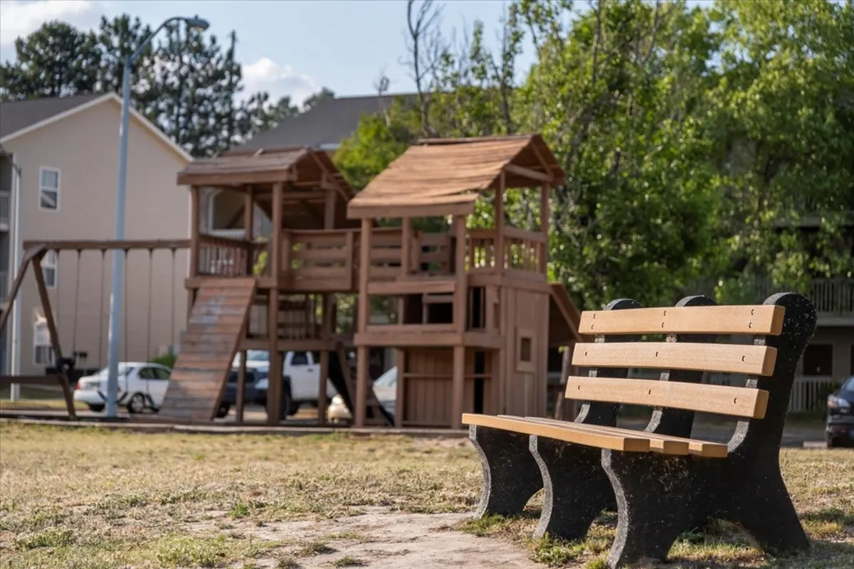 This exterior shot features a playground structure and a bench, set in a relaxed, open area. The mood is playful yet peaceful, offering a glimpse of community life and opportunities for picnicking or spending time outdoors, either with others or in solitude.