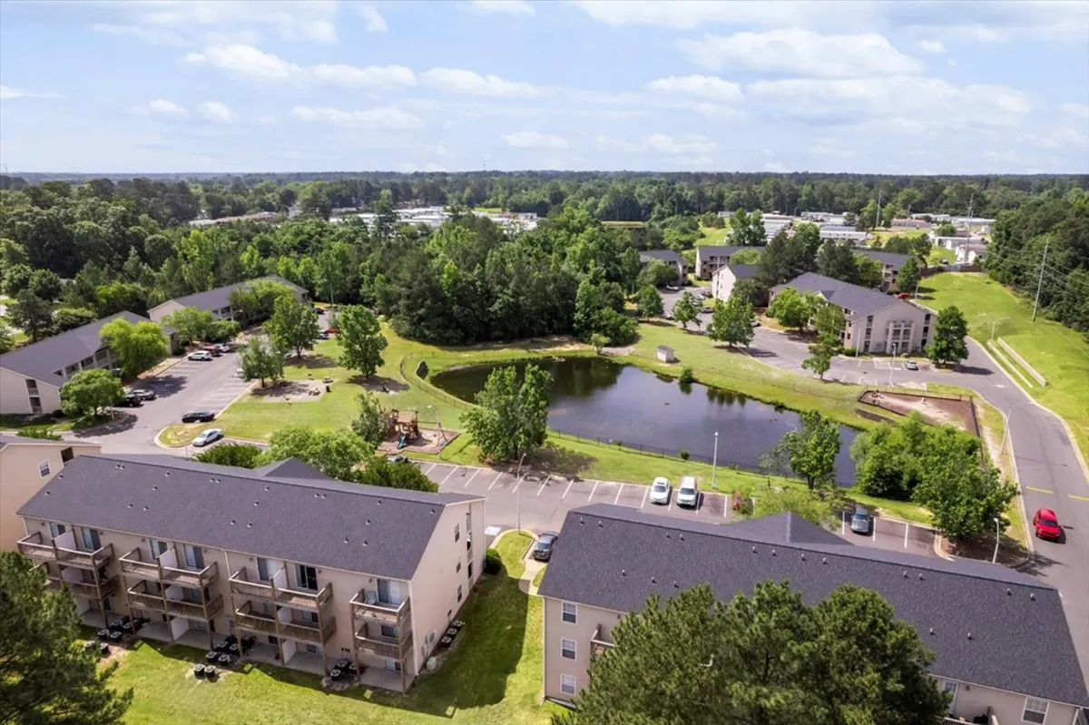 This exterior image captures a tranquil pond surrounded by lush greenery, with the apartment buildings in the background. The scene suggests a peaceful communal space ideal for walking, relaxing, or enjoying a quiet picnic after a day of exploring the city.